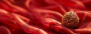 a close-up shot of a shiny, three-faced rudraksha bead resting on a bed of red silk fabric, highlighting its ancient and mystical origins.