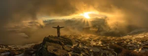 a person standing on a mountaintop, arms outstretched, basking in the golden rays of the rising sun.